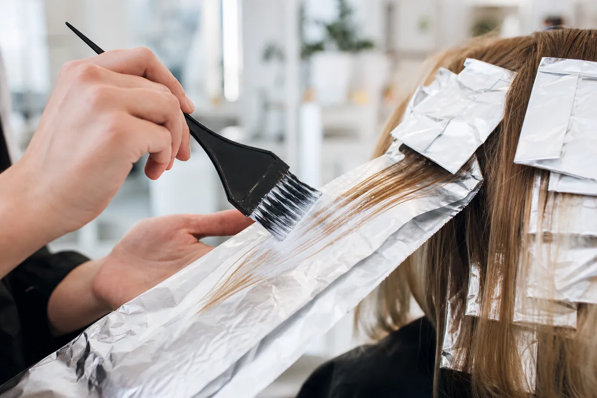 Coloriste appliquant un balayage cendré sur des mèches isolées sous papier aluminium, dans un salon lumineux